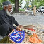 An elderly vendor displaying handmade items while sitting at roadside to attract the customers in Federal Capital.