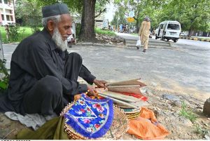 An elderly vendor displaying handmade items while sitting at roadside to attract the customers in Federal Capital.
