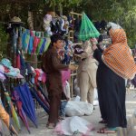 A woman purchasing umbrella from the roadside vendor during hot weather in the city.
