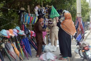 A woman purchasing umbrella from the roadside vendor during hot weather in the city.