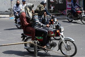 A motorcyclist covers his face with a scarf to shield against the soaring summer temperatures in the Provincial Capital