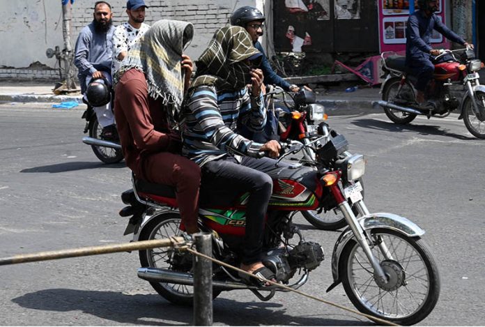 A motorcyclist covers his face with a scarf to shield against the soaring summer temperatures in the Provincial Capital