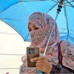 A woman shields herself with an umbrella to escape the blazing sun as extreme heat grips the federal capital