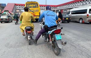 A police official on motorcycle helps an out of order motorcyclist by pushing with his foot to reach his destination.