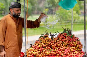 A vendor showers water on seasonal fruits (lychee) to keep them fresh near Eidgah.