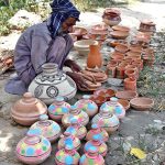 A vendor arranging and displaying clay made pots to attract the customers at his setup in the Federal Capital