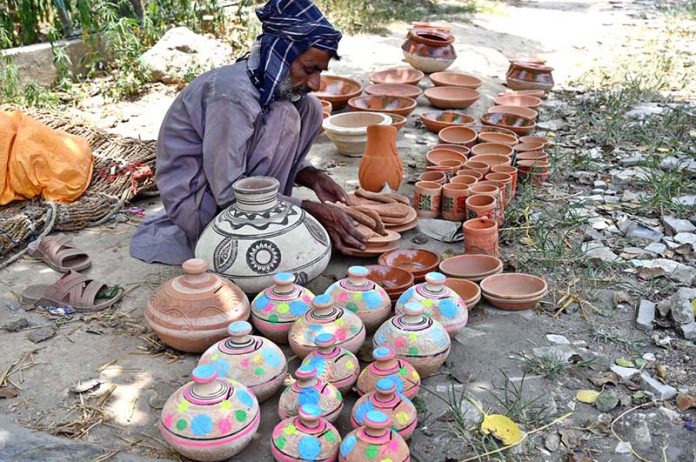 A vendor arranging and displaying clay made pots to attract the customers at his setup in the Federal Capital