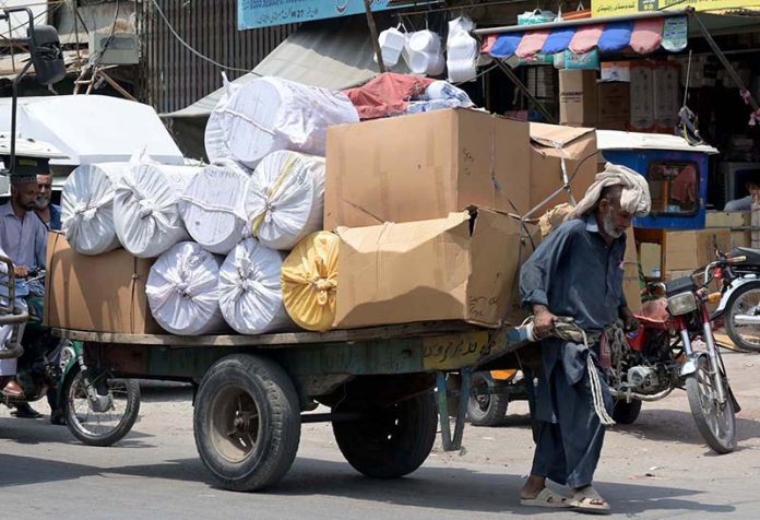 An elderly man pulls an overloaded cart with his full force through Raja Bazaar to earn a livelihood for his family under burning sun as temperatures soar in the city
