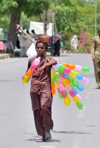 A young street vendor selling balloons while shuttling on the road.