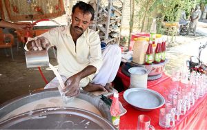 A young vendor preparing traditional summer drink (thadal) to attract the customers at roadside setup during hot weather in the city