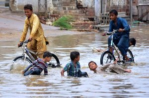 Girls passing through rain water accumulated on the road after heavy rain in the city at Makki Shah Road.