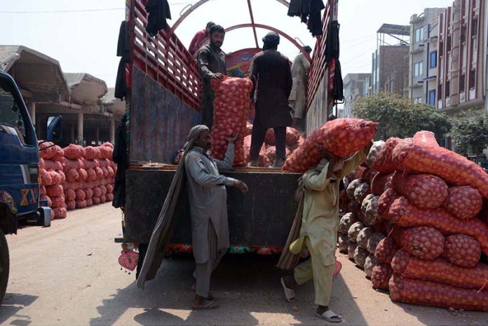 Laborers unloading onion filled bags from a delivery truck at vegetable market