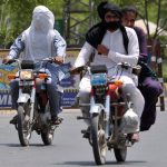 Motorcyclists covers their faces with a cloth to protect themselves from the scorching heat while riding along a City road