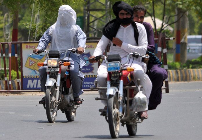 Motorcyclists covers their faces with a cloth to protect themselves from the scorching heat while riding along a City road