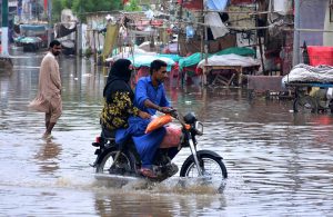 Girls passing through rain water accumulated on the road after heavy rain in the city at Makki Shah Road.
