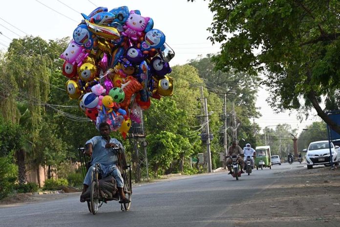 A differently-abled individual carries colorful balloon toys along Club Road in a bid to earn a livelihood