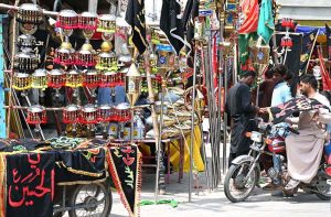 A Shia devotee on a motorcycle selects and purchases an Alam Pak of Imam Hussain (RA) from roadside stalls in preparation for Muharram-ul-Haram.