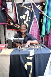 A Shia devotee on a motorcycle selects and purchases an Alam Pak of Imam Hussain (RA) from roadside stalls in preparation for Muharram-ul-Haram.