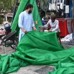 A worker sewing a green tarpaulin over machine to shield himself from the scorching heat at his workplace.
