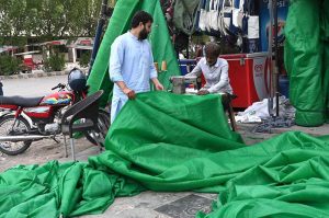 A worker sewing a green tarpaulin over machine to shield himself from the scorching heat at his workplace.
