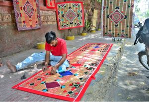 A worker crafts beautiful designs on a curtain chick and mats while selling on the footpath at Court Road