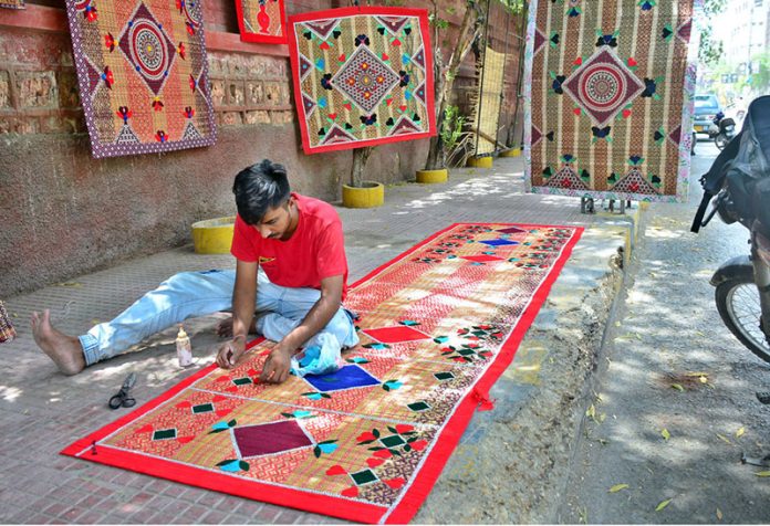 A worker crafts beautiful designs on a curtain chick and mats while selling on the footpath at Court Road