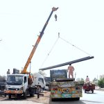 Labourers are busy unloading iron bars from a trailer using a crane at their workplace