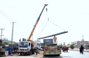 Labourers are busy unloading iron bars from a trailer using a crane at their workplace