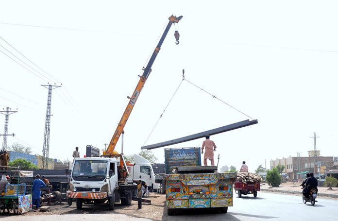 Labourers are busy unloading iron bars from a trailer using a crane at their workplace