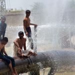 Youngsters enjoy bathing from leakage water pipe line over water canal during hot weather in the city