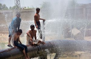 Youngsters enjoy bathing from leakage water pipe line over water canal during hot weather in the city