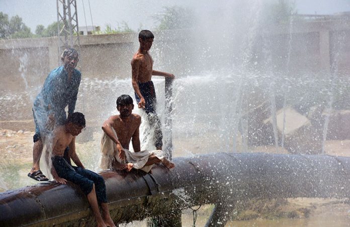 Youngsters enjoy bathing from leakage water pipe line over water canal during hot weather in the city