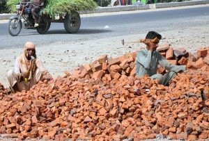 A labourer family crushes bricks with hammers for use in construction work along a roadside in the city.