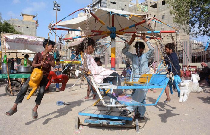 Children enjoy swing ride on the third day of Eid ul Azha at Chanesar Goth