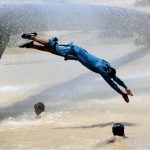 Youngsters enjoy bathing from leakage water pipe line over water canal during hot weather in the city