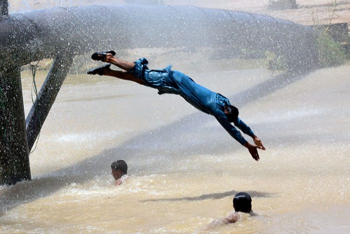 Youngsters enjoy bathing from leakage water pipe line over water canal during hot weather in the city