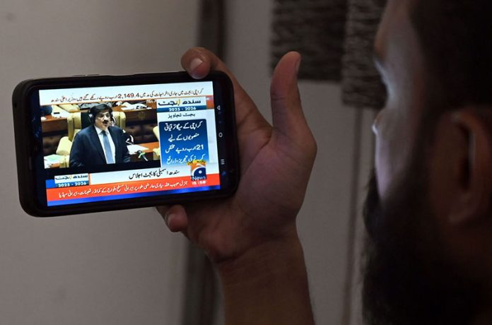 A citizen watches the live broadcast of the Sindh Budget 2025–26 on his mobile screen, presented by Sindh Chief Minister Syed Murad Ali Shah during the Sindh Assembly budget session