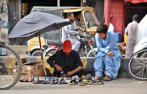 A cobbler repairs shoes for a customer on roadside his setup at Meezan Chowk.