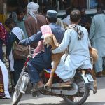 A person carries a sacrificial animal on a motorcycle while sitting on the pillion seat after purchasing it from the Animal Market for the upcoming Eid ul-Adha