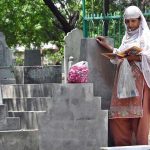 A woman recites verses from the Quran at the grave of her family member in a graveyard on the occasion of Eidul Azha