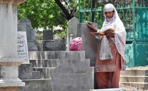 A woman recites verses from the Quran at the grave of her family member in a graveyard on the occasion of Eidul Azha