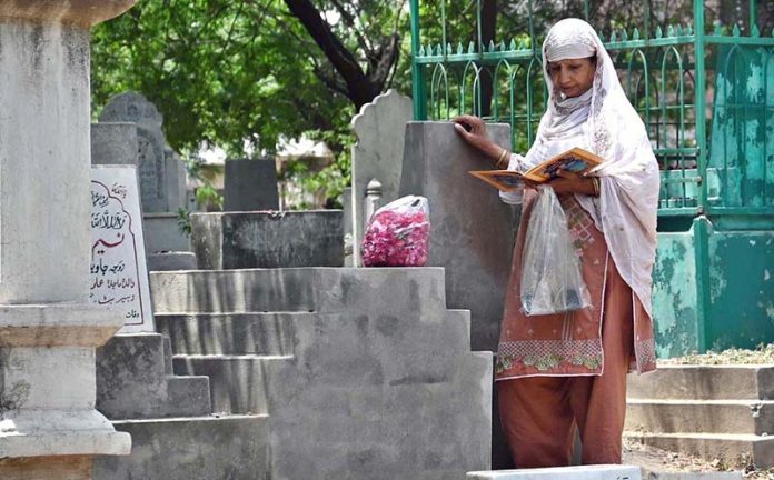 A woman recites verses from the Quran at the grave of her family member in a graveyard on the occasion of Eidul Azha