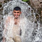 A young man enjoys a refreshing bath in a high-pressure stream to beat the scorching heat at Inqilab Road, Musazai area