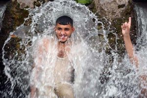 A young man enjoys a refreshing bath in a high-pressure stream to beat the scorching heat at Inqilab Road, Musazai area