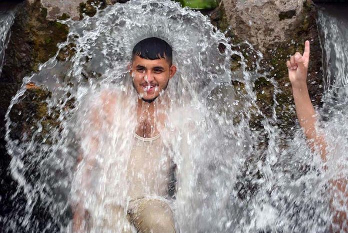 A young man enjoys a refreshing bath in a high-pressure stream to beat the scorching heat at Inqilab Road, Musazai area