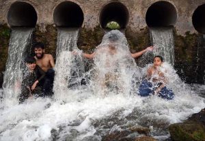 A young man enjoys a refreshing bath in a high-pressure stream to beat the scorching heat at Inqilab Road, Musazai area