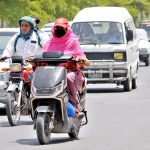 A woman confidently rides her scooter through the sun-drenched streets in the city.