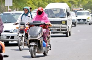 A woman confidently rides her scooter through the sun-drenched streets in the city.