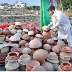 A vendor arranging and display clay pots to attract customers at his roadside setup.