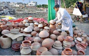 A vendor arranging and display clay pots to attract customers at his roadside setup.